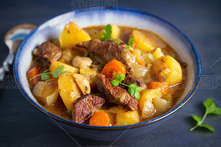 Beef meat stewed with potatoes, carrots and spices in bowl on dark gray background.  horizontal imag