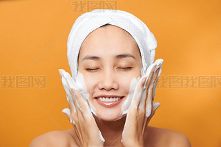 Happy young Asian woman applying face cream while wearing a towel and touching her face. Isolated on