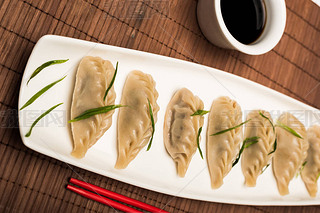 delicious Chinese boiled dumplings on plate near chopsticks and soy sauce on bamboo mat