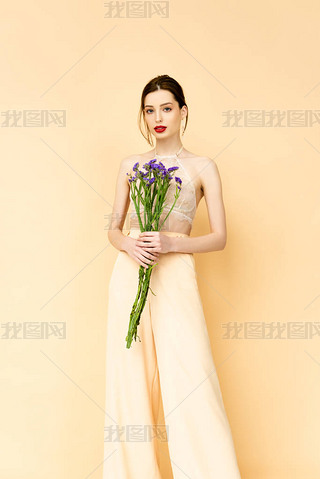 attractive woman holding purple limonium flowers and standing isolated on beige 