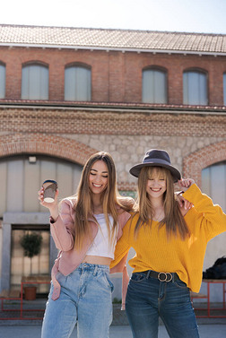 两个年轻的高加索女孩穿着温暖的春色衣服，在阳光下快乐地享受着大街上的美景