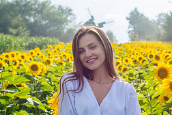 夏天，穿着白衬衫的美丽的微笑的年轻女子站在田野里的向日葵中间，背景是乡村的风景.