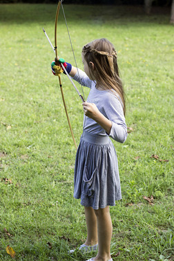 可爱的小女孩与辫子在蓝色礼服是玩弓和箭在草原上