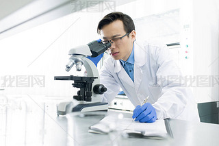 Asian medical scientist wearing white coat examining specimen using microscope, horizontal portrait