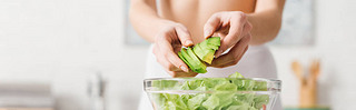Cropped view of fit woman cooking salad with juicy ocado in kitchen, panoramic shot