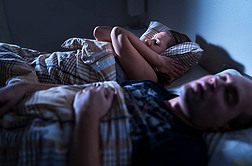 晚上打呼噜睡眠呼吸暂停。闷闷不乐的女人躺在床上用枕头捂住耳朵.妻子保持清醒。丈夫睡着了巨大的噪音。吵吵闹闹的人烦躁困倦的女士.