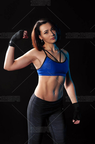 Beautiful young female athlete in blue sports top and leggings shows bitsipts. Black background. The