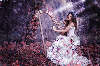 beautiful brown-haired woman with a flower wreath on her head, wearing a white dress playing the har