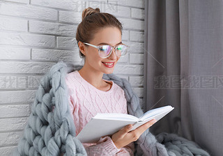 Young woman wearing knitted sweater with book at home