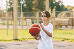 一个穿着白色T恤的漂亮少年站在篮球场上，手里拿着一个篮球。体育与健康生活方式的概念