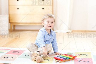 The boy plays xylophone at home. Cute iling positive boy playing with a toy musical instrument xyl