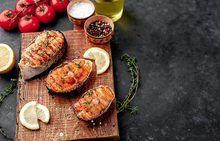 Three grilled salmon steaks with spices, lemon and tomatoes on a stone background