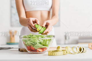 Cropped view of slim woman cooking salad with fresh vegetables and ocado near measuring tape on ki