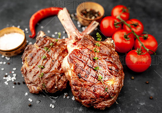 grilled beef steaks - tomahawk with tomatoes and red pepper on a stone background