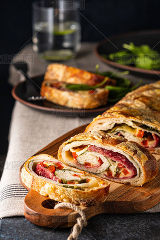 Traditional Italian Stromboli stuffed with cheese, salami, red pepper and spinach. Photo in a dark s