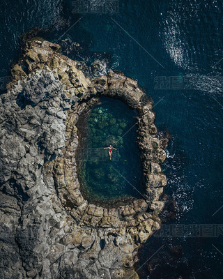 Beautiful girl in a red swimsuit swims in a round natural pool. Top view of a drone on a girl in a p