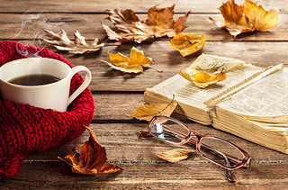 Hot coffee, vintage book, glasses and autumn lees on wood