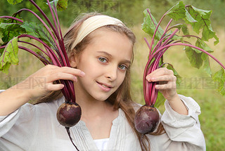 white girl of 10 years old holds 2 beets in her hands on a background of greenery