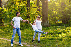 快乐的小女孩跳跃牵手与父母走在阳光明媚的公园, 全长