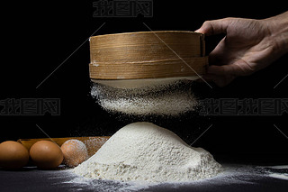 Flour is sifted through a sieve on a black background. Flour of the highest grade on a dark backgrou