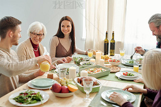 Young man pouring orange juice for his granny during family dinner by served festive table on Thanks