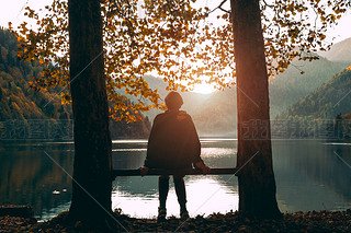 A girl sits on a bench and looks at Lake Ritsa at sunset in Abkhazia. Mountain landscape