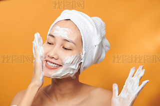 Close up beauty portrait of a laughing beautiful half naked Asian woman applying face cream and look
