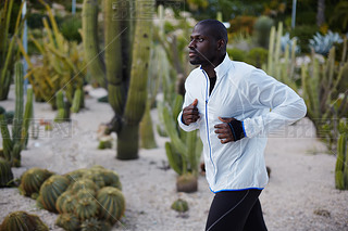 Young fit man in white windbreaker running fast in beautiful park, autumn sport outdoors, attractive