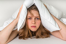 在噪音遮住耳朵用枕头的床上的女人