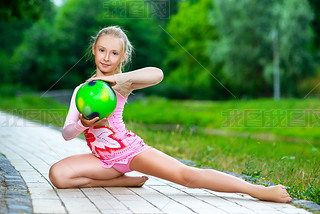outdoor portrait of young cute little girl gymnast training with ball in park