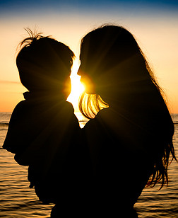 母亲和儿子在一个深的时刻爱日落期间在海滩-一个年轻的妈妈和他可爱的孩子之间的联盟和投标连接概念-修改的形状的轮廓与筛选器的太阳耀光