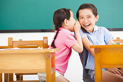 快乐的小女孩耳语和分享在教室里的秘密