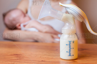 Manual breast pump with milk, mother and baby at background