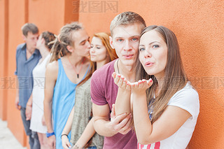 Group of happy young people standing near wall and kissing