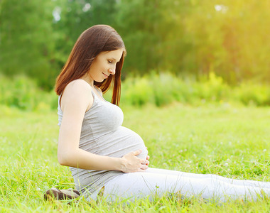 Portrait of happy pregnant woman sitting on the grass enjoys sun