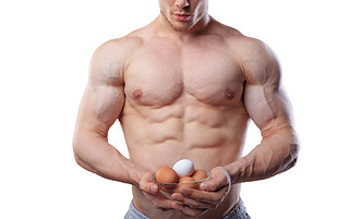 Shirtless athlete man showing cup with eggs at isolated white background