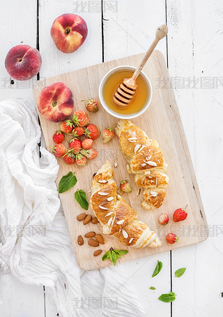 Freshly baked almond croissants with garden strawberries, peaches, mint and honey on serving board o