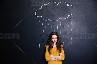 Unpleased woman with raincloud drawn over her on blackboard background 