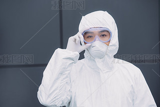 asian epidemiologist in hazmat suit and respirator mask looking at camera while standing outside and