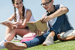 在公园里用书和数码片学习微笑的青少年男孩和女孩的镜头