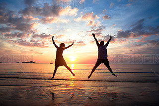 Concept of long-awaited vacation: Young couple in a jump on the sea beach at sunset.
