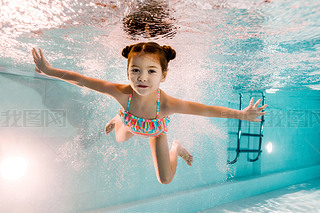 adorable kid swimming underwater in blue water in swimming pool 