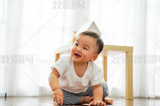 One lovely male infant laughing and hing fun in living room against white windows. He can sit on t