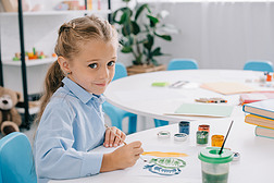 可爱的孩子坐在桌子上, 油漆和油漆刷的侧面视图 
