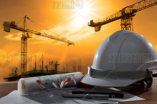 Safety helmet and architect pland on wood table with sunset scen