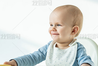 Smiling baby boy with soiled mouth sitting on feeding chair on white background