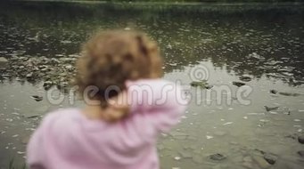 金发卷曲的小女孩在河里扔石头 山脉背景
