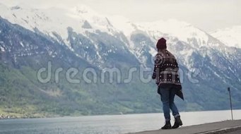 穿着花纹外套和针织帽子的女人在湖边用面包喂鸟