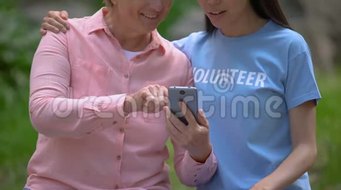 快乐的老年妇女向年轻志愿者展示智能手机照片交流